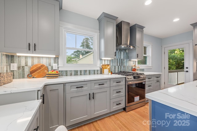 2421 Morton St, Charlotte, NC 28208 - kitchen featuring stainless steel gas stove, wall chimney exhaust hood, gray cabinetry, light wood-type flooring, and decorative backsplash