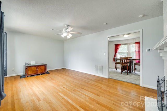 2111 Parkdale Ave, Gastonia, NC 28052 - unfurnished living room with ceiling fan, light wood-type flooring, a textured ceiling, a fireplace, and baseboards