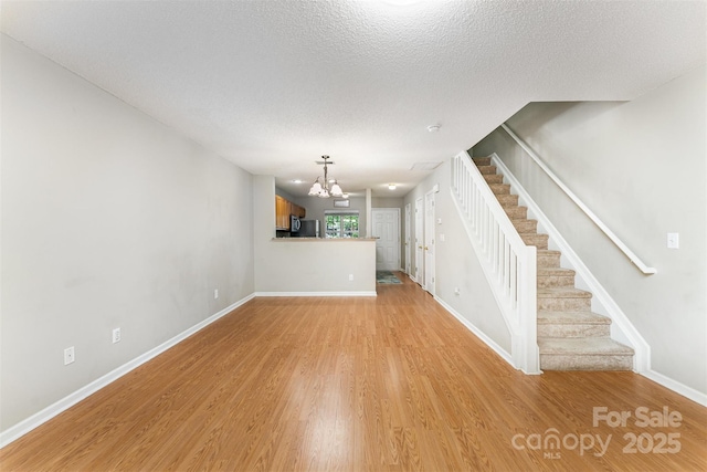 10223 Reindeer Way Ln, Charlotte, NC 28216 - unfurnished living room featuring a chandelier, stairs, light wood-style flooring, baseboards, and a textured ceiling