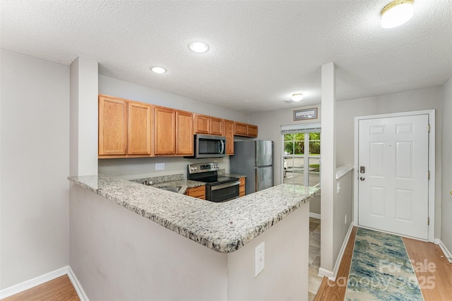 10223 Reindeer Way Ln, Charlotte, NC 28216 - kitchen featuring stainless steel appliances, a peninsula, a textured ceiling, light wood-style flooring, and light stone counters