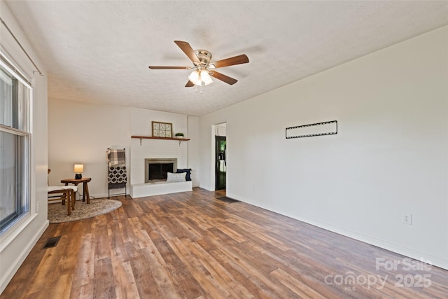 40 Autumn St, Canton, NC 28716 - unfurnished living room with wood finished floors, ceiling fan, a fireplace with raised hearth, baseboards, and a textured ceiling