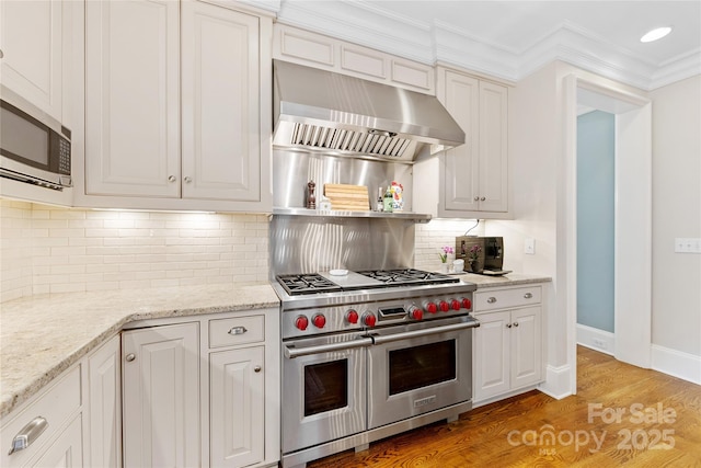 1728 Shadow Forest Dr, Matthews, NC 28105 - kitchen featuring appliances with stainless steel finishes, wall chimney range hood, light wood finished floors, white cabinetry, and ornamental molding