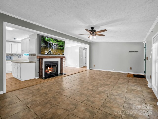 2941 Nix Creek Rd, Marion, NC 28752 - unfurnished living room featuring a ceiling fan, tile patterned floors, crown molding, a warm lit fireplace, and a textured ceiling