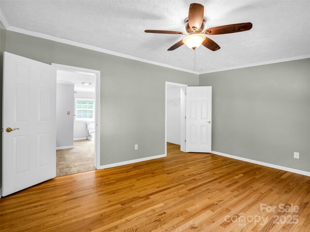 2941 Nix Creek Rd, Marion, NC 28752 - unfurnished bedroom featuring light wood-style flooring, a textured ceiling, a walk in closet, crown molding, and baseboards