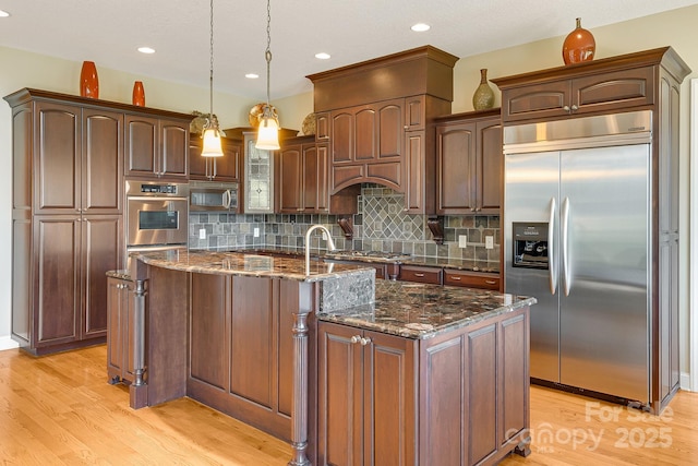 122 Eagles Crest Way, Lake Lure, NC 28746 - kitchen featuring stainless steel appliances, light wood-style flooring, decorative backsplash, dark stone counters, and a center island with sink
