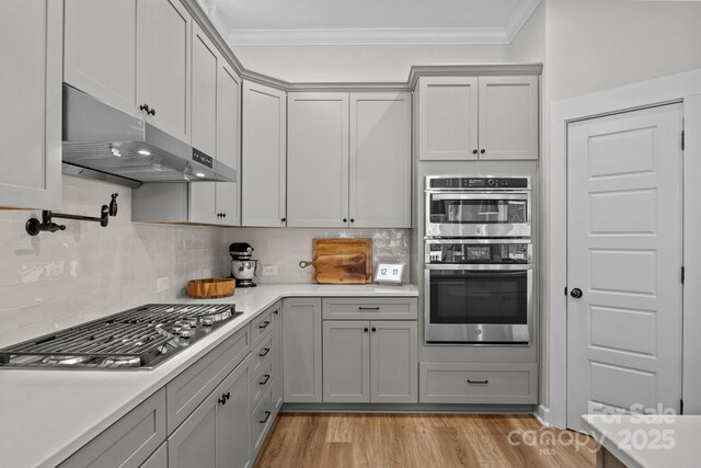 11329 Fullerton Place Dr NW, Huntersville, NC 28078 - kitchen with stainless steel appliances, ornamental molding, under cabinet range hood, gray cabinetry, and light countertops