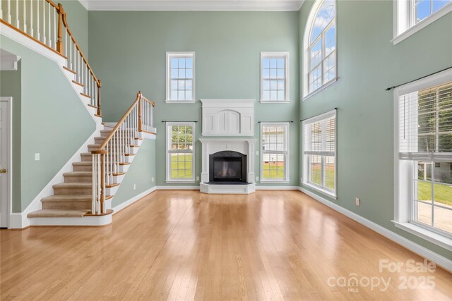 112 Doyle Farm Ln, Mooresville, NC 28115 - unfurnished living room with a glass covered fireplace, hardwood / wood-style flooring, baseboards, a towering ceiling, and stairway