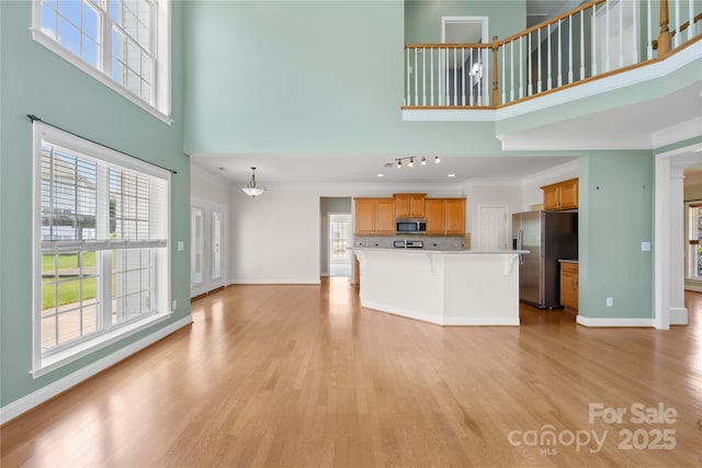 112 Doyle Farm Ln, Mooresville, NC 28115 - unfurnished living room featuring a towering ceiling, light wood finished floors, ornamental molding, healthy amount of natural light, and baseboards