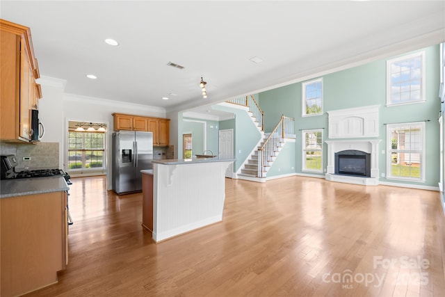 112 Doyle Farm Ln, Mooresville, NC 28115 - kitchen featuring appliances with stainless steel finishes, a glass covered fireplace, crown molding, decorative backsplash, and a kitchen breakfast bar