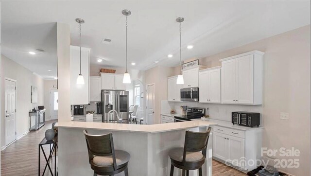 2009 Trindle Vine Ln, Waxhaw, NC 28173 - kitchen with stainless steel appliances, a breakfast bar area, light wood-style floors, white cabinets, and recessed lighting
