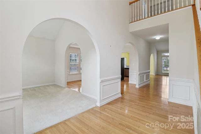 2321 Oberwood Dr, Charlotte, NC 28270 - unfurnished room featuring light wood-type flooring, wainscoting, arched walkways, a decorative wall, and a towering ceiling