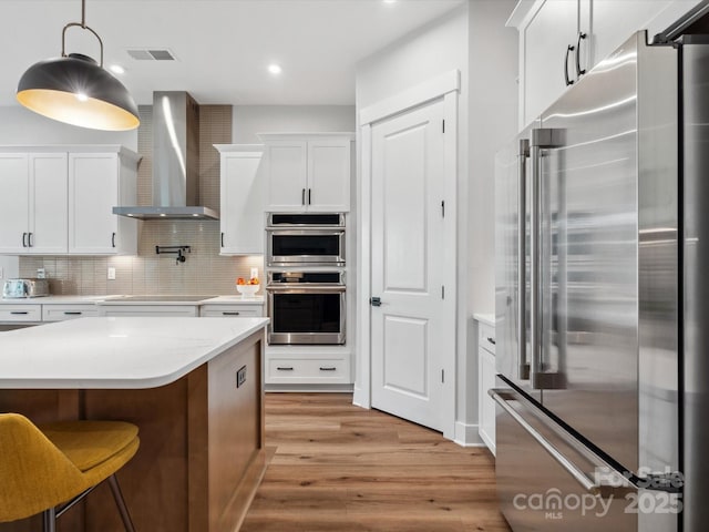6020 Waldorf Ave, Monroe, NC 28110 - kitchen with stainless steel appliances, wall chimney exhaust hood, light wood-style floors, white cabinets, and recessed lighting