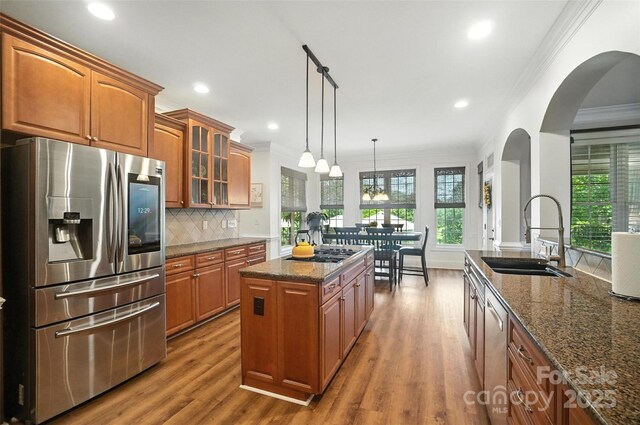 5916 Four Wood Dr, Matthews, NC 28104 - kitchen with stainless steel appliances, arched walkways, brown cabinets, dark stone countertops, and ornamental molding