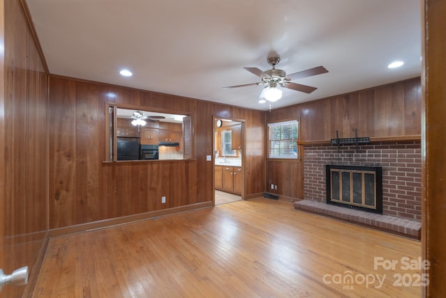 5720 Amity Pl, Charlotte, NC 28212 - unfurnished living room with wood walls, a ceiling fan, a brick fireplace, light wood-style floors, and recessed lighting