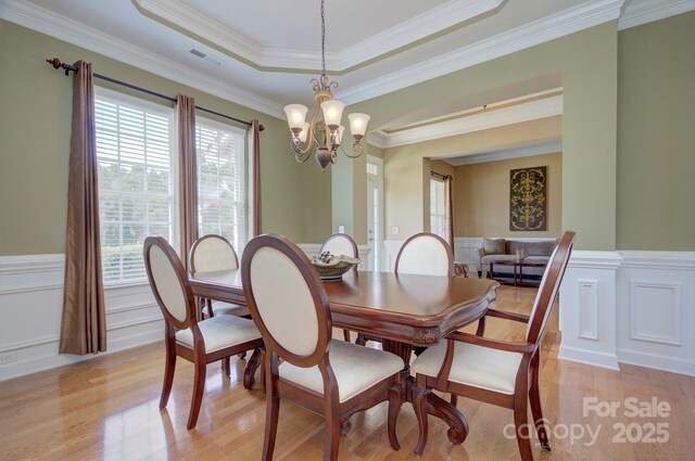 604 Palmerston Ln, Waxhaw, NC 28173 - dining area with light wood-style floors, a chandelier, a wainscoted wall, crown molding, and a tray ceiling