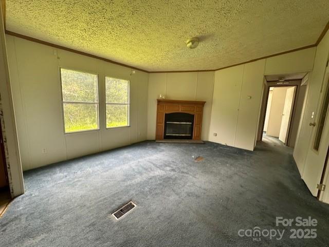 5587 Doe Ct, Morganton, NC 28655 - unfurnished living room featuring a textured ceiling, a fireplace with raised hearth, ornamental molding, carpet, and a decorative wall