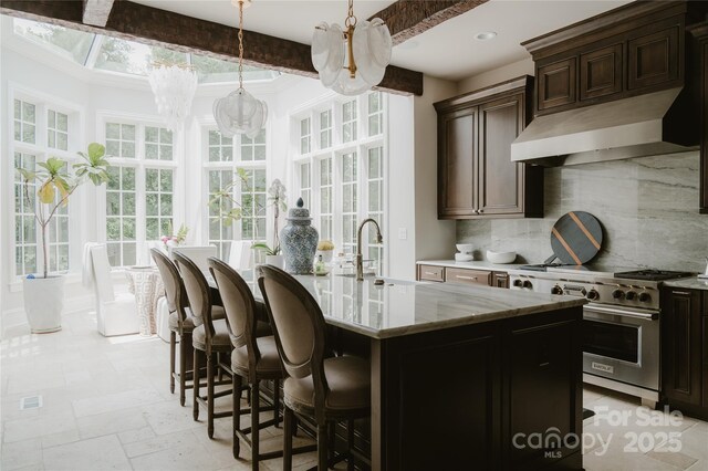 8500 Longview Club Dr, Waxhaw, NC 28173 - kitchen featuring high end stainless steel range, premium range hood, backsplash, light stone countertops, and a kitchen island with sink