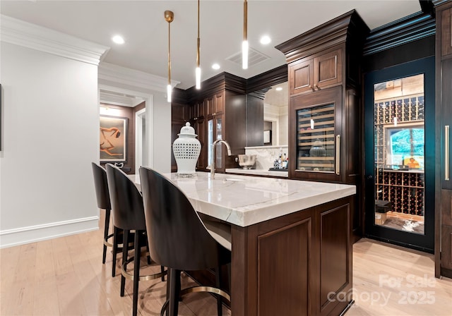 8500 Longview Club Dr, Waxhaw, NC 28173 - kitchen featuring wine cooler, ornamental molding, light wood finished floors, light stone counters, and an island with sink