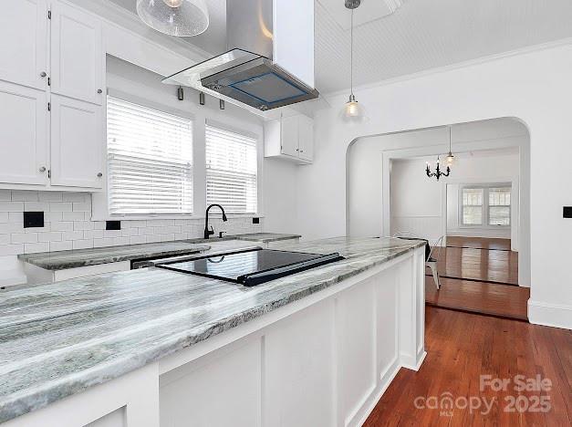12300 Caldwell Rd, Charlotte, NC 28213 - kitchen with black electric stovetop, wall chimney exhaust hood, white cabinets, light stone counters, and decorative light fixtures