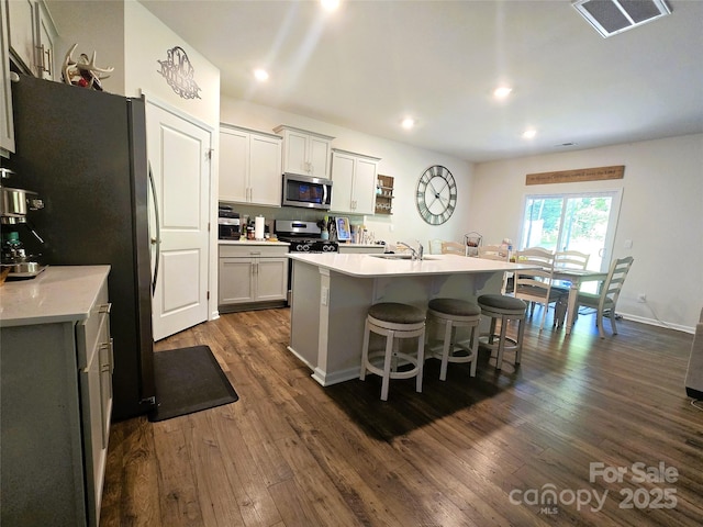 3816 Rosewood Dr, Mount Holly, NC 28120 - kitchen with appliances with stainless steel finishes, a breakfast bar area, dark wood-style floors, light countertops, and an island with sink