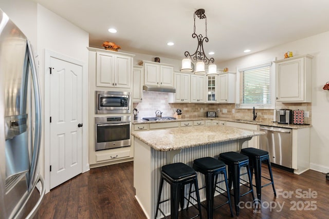 274 Cove Creek Loop, Mooresville, NC 28117 - kitchen featuring appliances with stainless steel finishes, under cabinet range hood, a kitchen bar, decorative backsplash, and dark wood-type flooring
