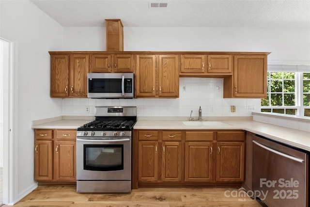 13832 Queenswater Ln, Charlotte, NC 28273 - kitchen with stainless steel appliances, a sink, brown cabinetry, and a textured ceiling