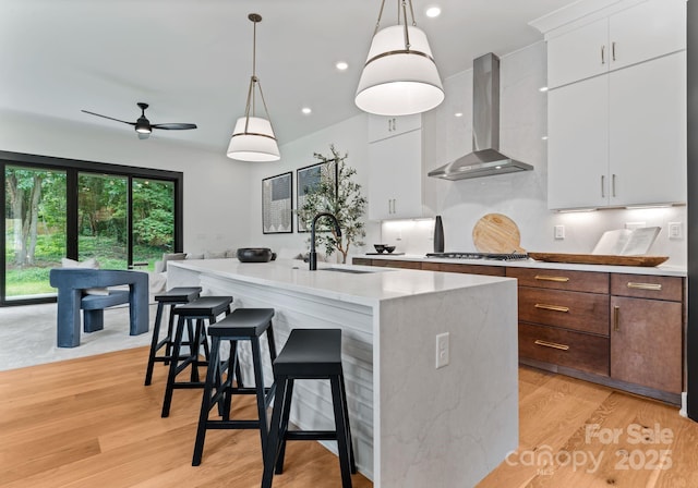 4117 Sarah Dr, Charlotte, NC 28217 - kitchen with wall chimney range hood, white cabinetry, a breakfast bar area, a kitchen island with sink, and decorative light fixtures