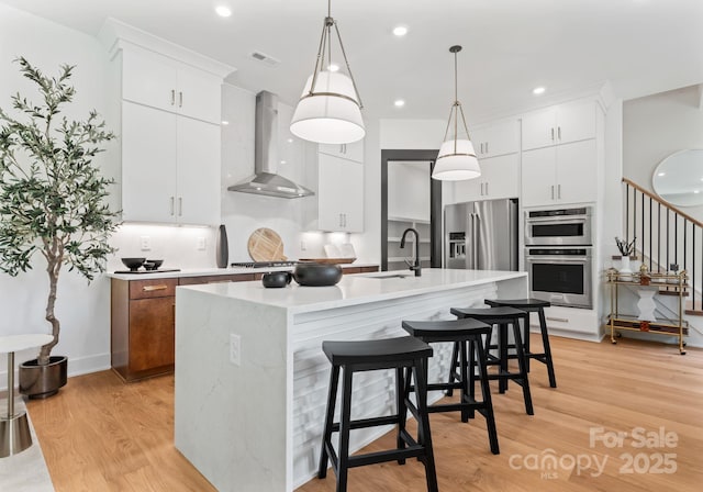 4117 Sarah Dr, Charlotte, NC 28217 - kitchen featuring wall chimney exhaust hood, appliances with stainless steel finishes, light wood-type flooring, light countertops, and an island with sink