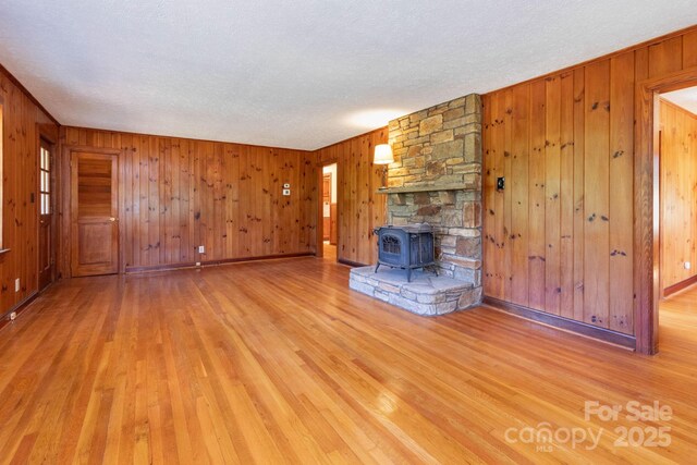 18 Gravely Branch Rd, Fletcher, NC 28732 - unfurnished living room with wooden walls, a wood stove, a textured ceiling, and light wood-style flooring