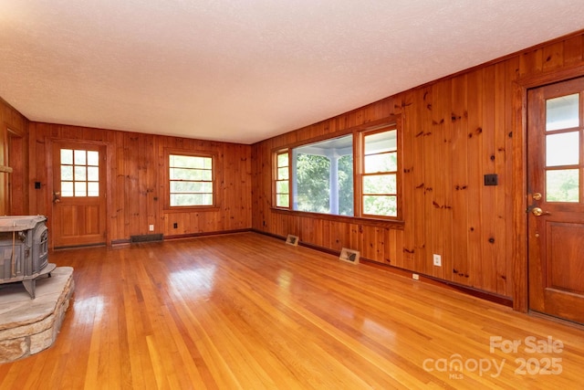 18 Gravely Branch Rd, Fletcher, NC 28732 - unfurnished living room featuring light wood-style floors, a wood stove, a textured ceiling, and wood walls