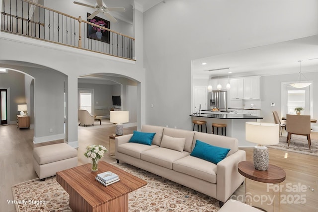 122 Long Cove Ln, Mooresville, NC 28117 - living room with a ceiling fan, light wood-style flooring, arched walkways, a towering ceiling, and baseboards