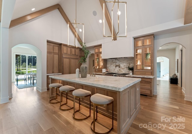 15037 June Washam Rd, Davidson, NC 28036 - kitchen featuring brown cabinets, high vaulted ceiling, arched walkways, a kitchen breakfast bar, and a large island