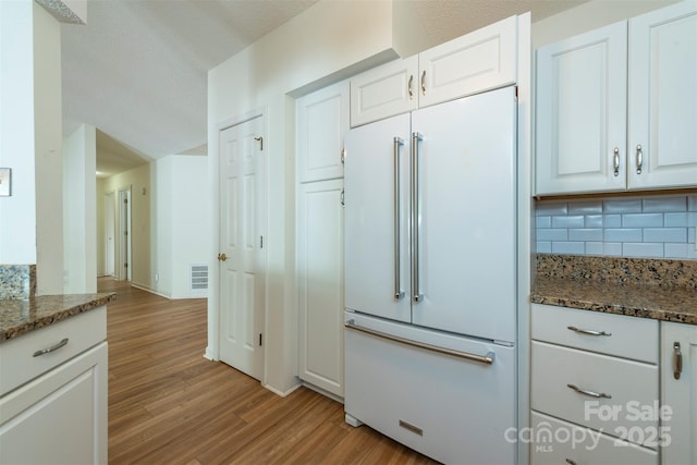 16 Red Barn Ln, Fletcher, NC 28732 - kitchen featuring paneled built in fridge, light wood-type flooring, backsplash, white cabinets, and dark stone counters