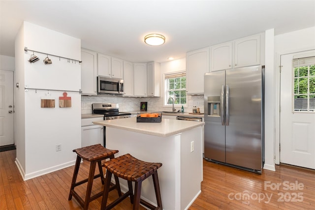 1912 Baxter St, Charlotte, NC 28204 - kitchen with appliances with stainless steel finishes, a kitchen breakfast bar, light wood finished floors, white cabinetry, and healthy amount of natural light
