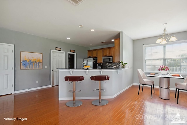 8915 Merrie Rose Ave, Charlotte, NC 28213 - kitchen featuring appliances with stainless steel finishes, brown cabinetry, light wood finished floors, a chandelier, and a peninsula