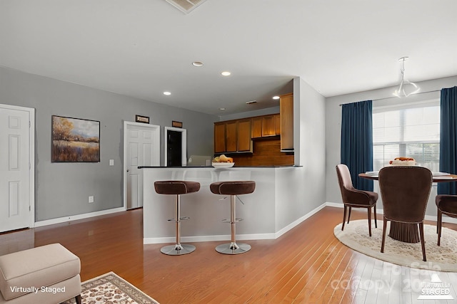 8915 Merrie Rose Ave, Charlotte, NC 28213 - kitchen with light wood-style floors, brown cabinets, a peninsula, recessed lighting, and a breakfast bar area