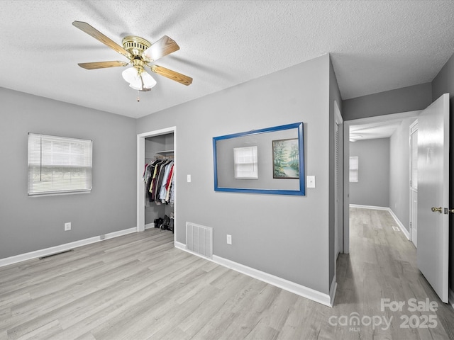 3509 Flint Dr, Statesville, NC 28677 - unfurnished bedroom featuring light wood finished floors, a textured ceiling, a closet, a ceiling fan, and a walk in closet
