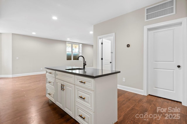 4015 Randolph Rd, Charlotte, NC 28211 - kitchen with dark countertops, wood finished floors, recessed lighting, an island with sink, and white cabinets