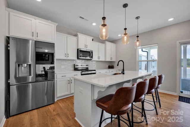 1315 Elizabeth Ave, Kannapolis, NC 28083 - kitchen featuring appliances with stainless steel finishes, light wood finished floors, a kitchen island with sink, light countertops, and white cabinets