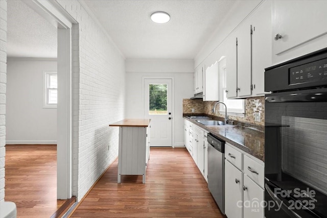 1512 Anthony Dr, Gastonia, NC 28052 - kitchen with oven, stainless steel dishwasher, light wood-style flooring, white cabinets, and brick wall