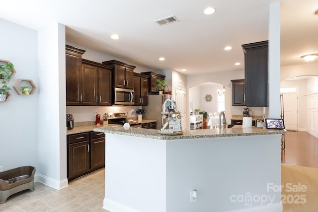 2405 Emma Grace Ln, Rock Hill, SC 29732 - kitchen featuring stainless steel appliances, arched walkways, dark brown cabinetry, recessed lighting, and light stone countertops