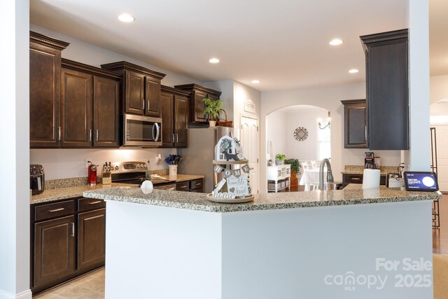 2405 Emma Grace Ln, Rock Hill, SC 29732 - kitchen with appliances with stainless steel finishes, arched walkways, dark brown cabinetry, recessed lighting, and light stone countertops