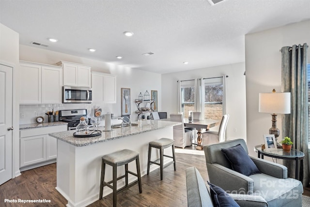 3908 Coleman Dr, Charlotte, NC 28215 - kitchen with appliances with stainless steel finishes, dark wood-type flooring, white cabinetry, a kitchen breakfast bar, and recessed lighting