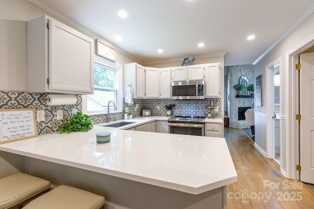 27092 Village Dr, Tega Cay, SC 29708 - kitchen with appliances with stainless steel finishes, a peninsula, light countertops, a kitchen bar, and light wood-style floors