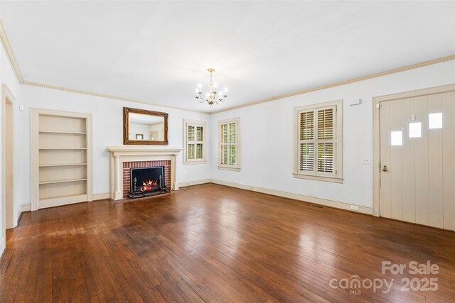 805 S Main St, Mount Holly, NC 28120 - unfurnished living room featuring built in shelves, a chandelier, hardwood / wood-style flooring, a brick fireplace, and crown molding