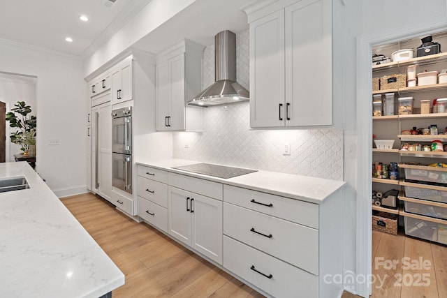 8283 Long Island Rd, Catawba, NC 28609 - kitchen featuring wall chimney range hood, black electric stovetop, ornamental molding, light wood-style floors, and white cabinetry