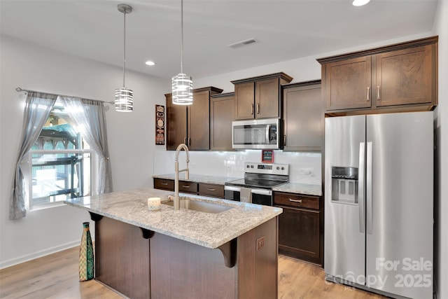 112 Aspire Cir, Wingate, NC 28174 - kitchen with appliances with stainless steel finishes, dark brown cabinetry, light stone counters, a center island with sink, and recessed lighting