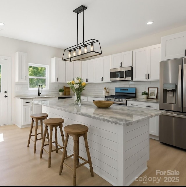 5526 Brookwood Ln, Hickory, NC 28602 - kitchen with appliances with stainless steel finishes, a center island, light wood-type flooring, light stone counters, and decorative backsplash