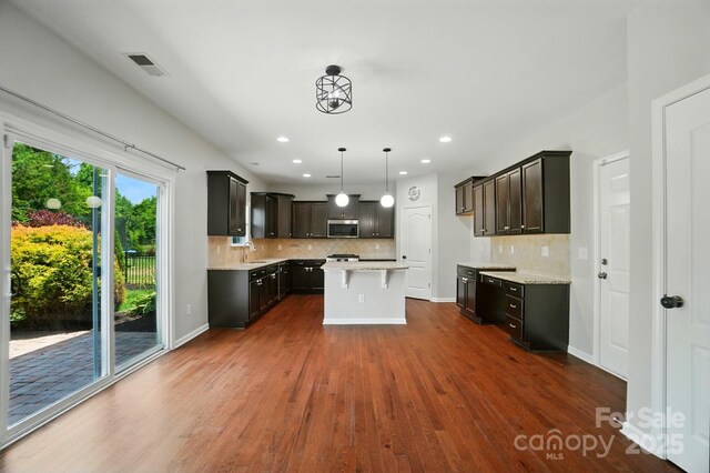 8115 Kelburn Ln, Charlotte, NC 28273 - kitchen featuring stainless steel microwave, dark wood-style floors, decorative backsplash, a center island, and recessed lighting