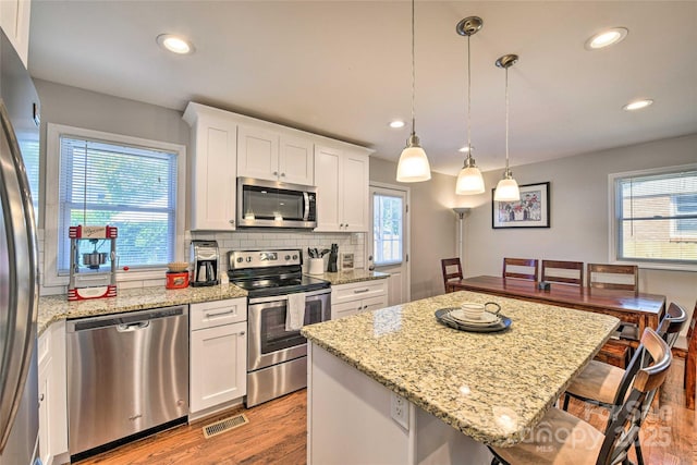 3020 Stancill Pl, Charlotte, NC 28205 - kitchen with appliances with stainless steel finishes, a breakfast bar area, light wood-type flooring, white cabinetry, and a center island